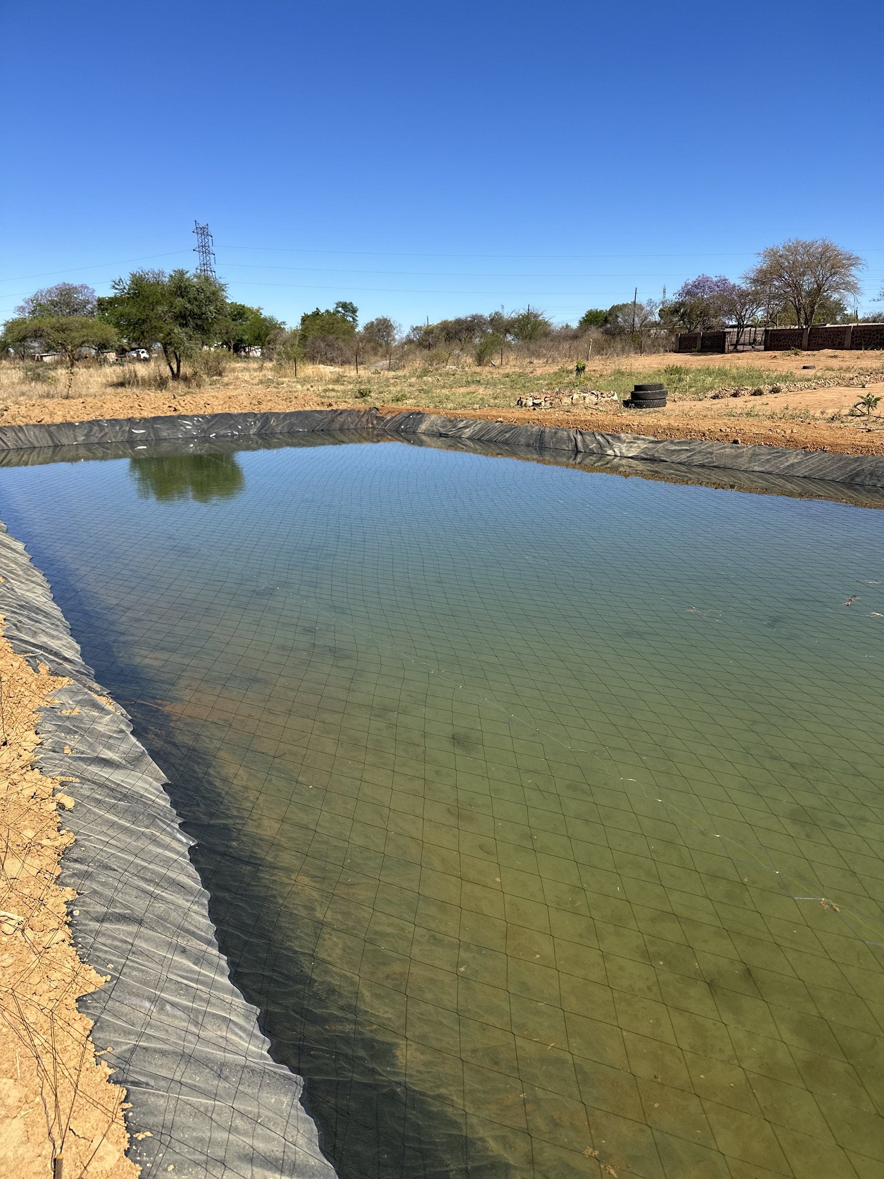 A finished lined pond full of water under a blue sky