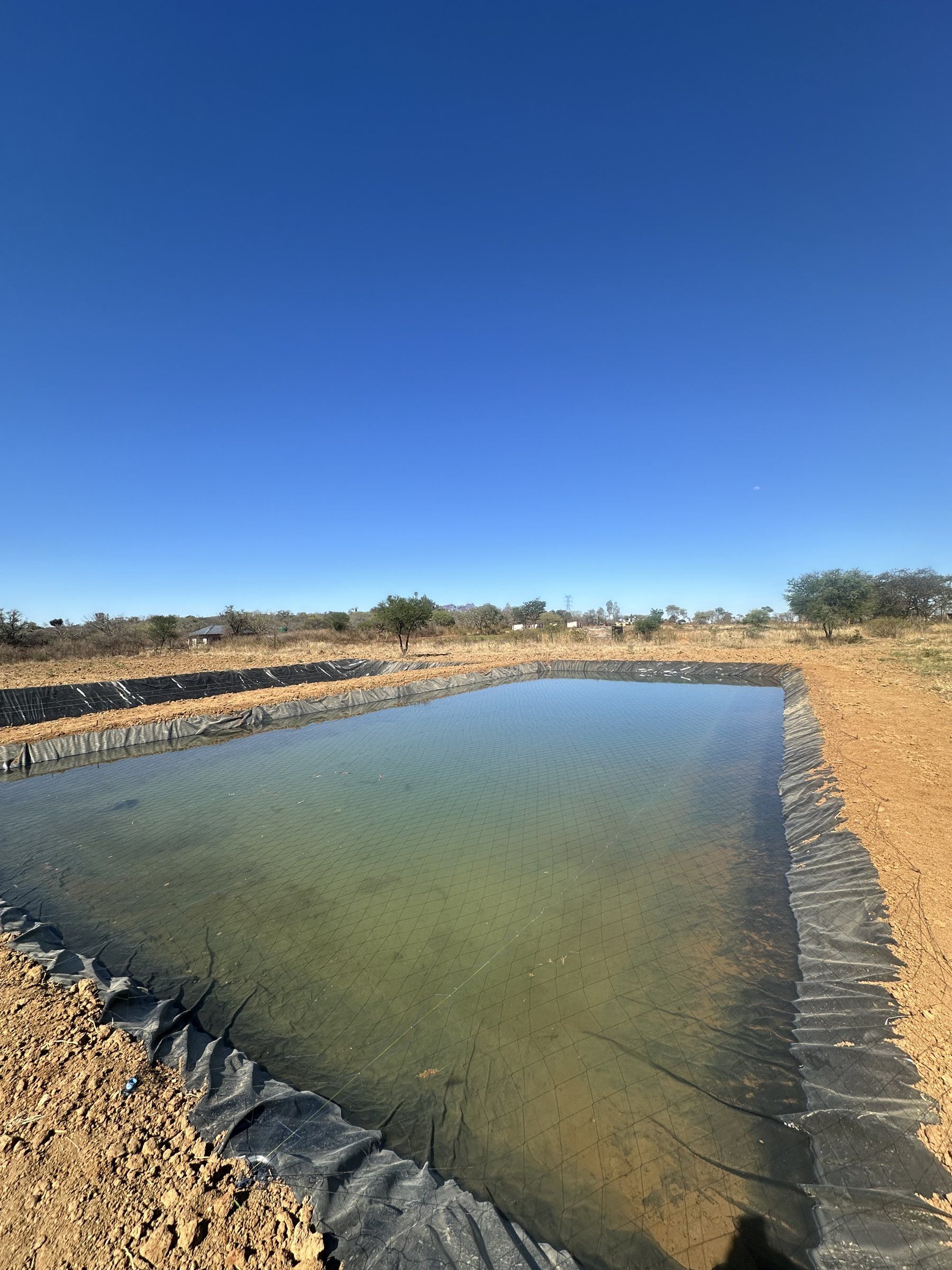 A finished lined pond full of water under a blue sky